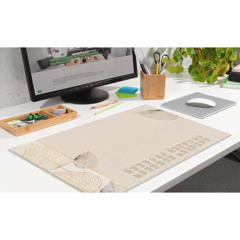 Ein aufgeräumter Arbeitsplatz mit einem Monitor, einer Schreibunterlage und Schreibwaren. Auf dem Bildschirm wird eine Website mit grünen Akzenten angezeigt. Eine Pflanze sorgt für Grün.