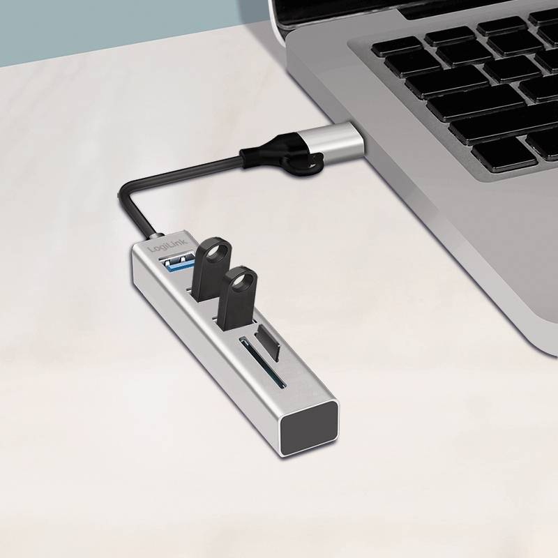 Ein Laptop mit einem angeschlossenen USB-Hub, der mehrere USB-Anschlüsse und angeschlossene Geräte aufweist, der auf einem hellen Schreibtisch steht.