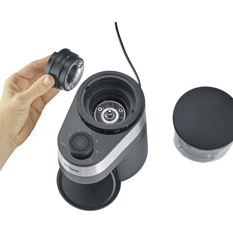 Eine Person hält den abnehmbaren Deckel einer kompakten elektrischen Kaffeemühle, während ein weiterer Deckel in der Nähe auf einer weißen Oberfläche liegt.