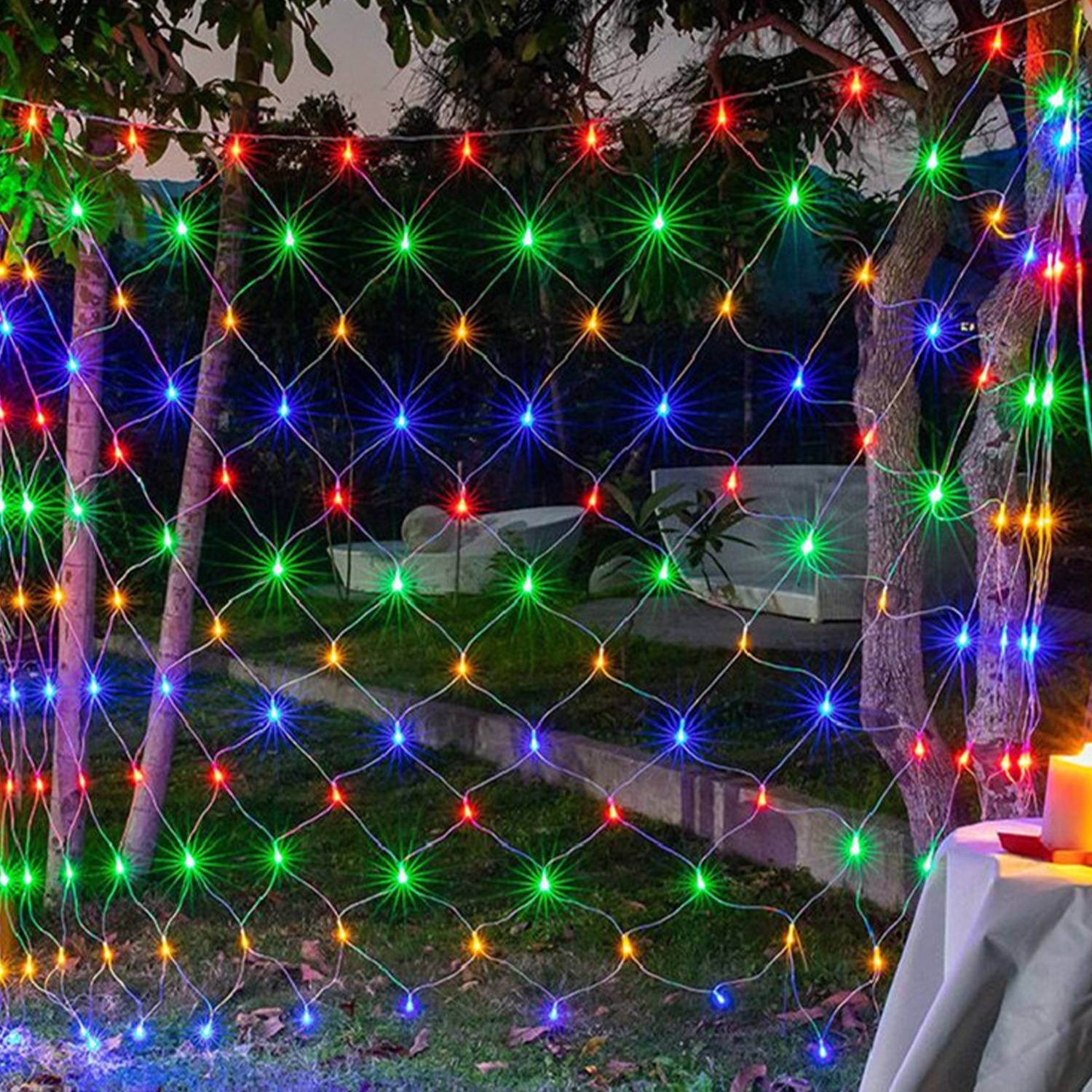 Farbenfrohe Lichterketten bilden ein Netz zwischen Bäumen in einem Garten in der Nacht, mit hell leuchtenden mehrfarbigen Punkten, die über eine dunkle Außenszene strahlen.