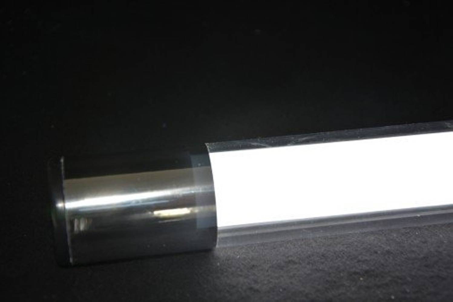 Eine Nahaufnahme einer fluoreszierenden Leuchtstoffröhre, die hell vor einem dunklen Hintergrund leuchtet und ihre zylindrische Form hervorhebt.