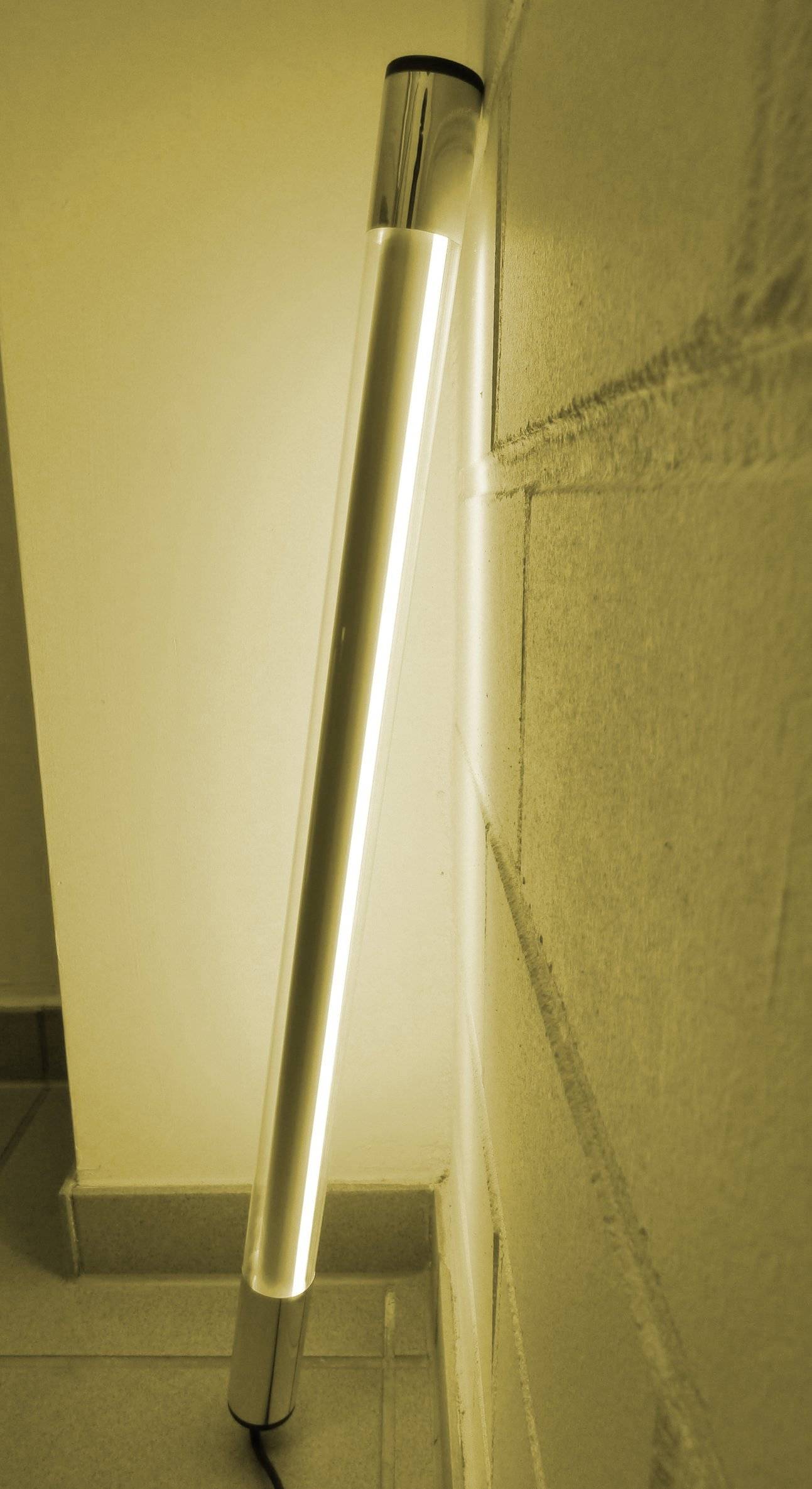 Ein vertikaler, gelb beleuchteter LED-Streifen verläuft entlang der Kante einer Betonwand und wirft ein weiches Licht auf die Oberfläche.