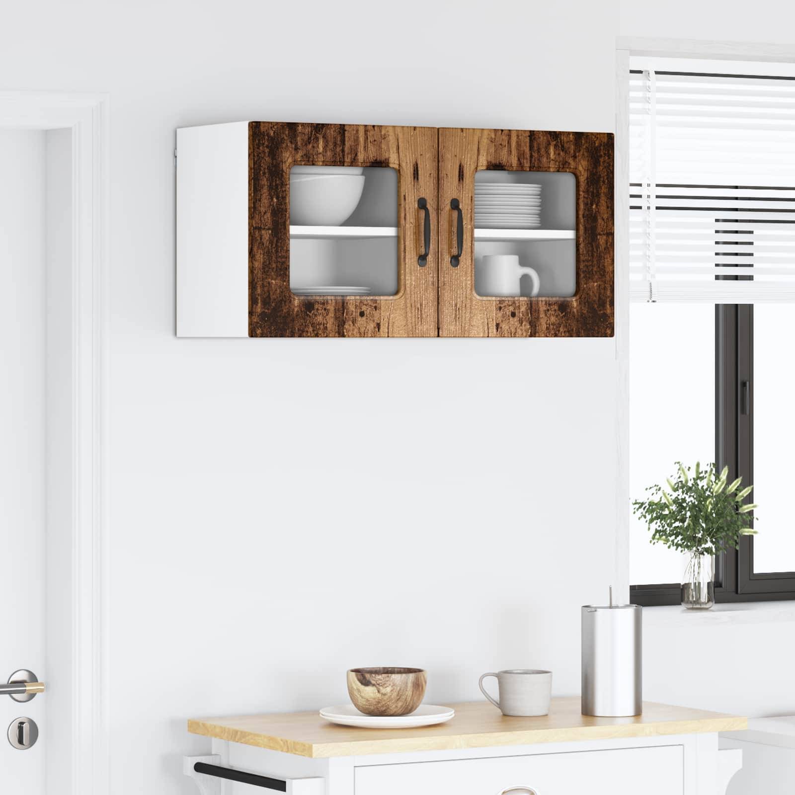 Eine minimale Küchenszene mit einem weißen Schrank und Holztüren an der Wand. Darunter steht ein kleiner Tisch mit einer Schüssel, einer Tasse und einem Glas.