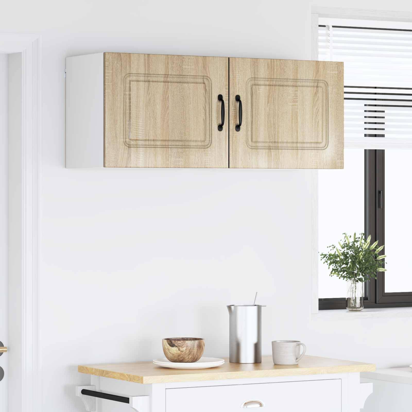 Holzküchenschrank mit schwarzen Griffen an einer weißen Wand montiert. In der Nähe eine Arbeitsfläche mit einer Holzschüssel, einem Metallbehälter und einer Tasse.