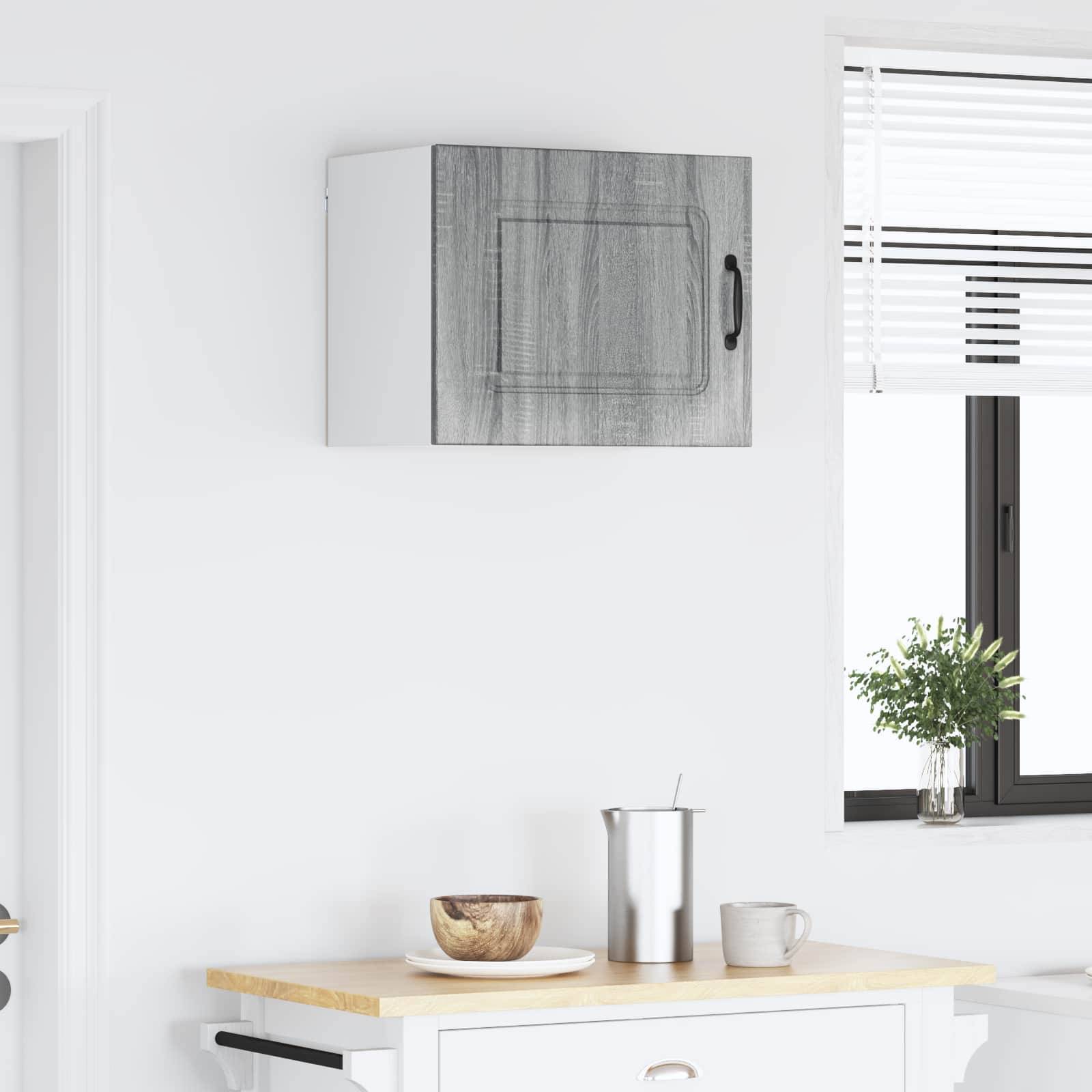 Eine minimalistische Küchenszene mit einer kleinen Holzarbeitsplatte, auf der sich eine Schüssel, ein metallischer Krug und eine Tasse befinden. Ein Fenster mit Jalousien und einer kleinen Topfpflanze auf dem Fenstersims sorgt für natürliches Licht.