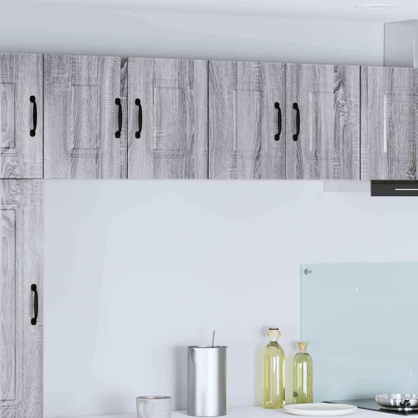 Eine Küche mit Holzschränken, einer Edelstahlkanne und zwei grünen Glasflaschen auf einer weißen Arbeitsplatte.