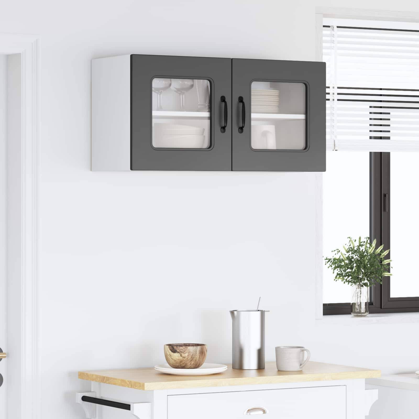 Moderner Küchenwandhängeschrank mit Glastüren über einer hellen Arbeitsplatte, auf der eine Schüssel, eine Tasse und ein Besteckbehälter in der Nähe eines Fensters stehen.