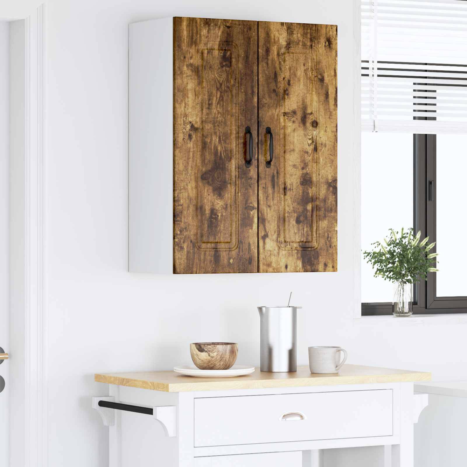 Ein an der Wand befestigter Schrank mit Holztüren hängt über einer weißen Küchenarbeitsplatte, auf der eine Schüssel, ein Metalltopf und eine Tasse stehen. Rechts befindet sich ein Fenster.