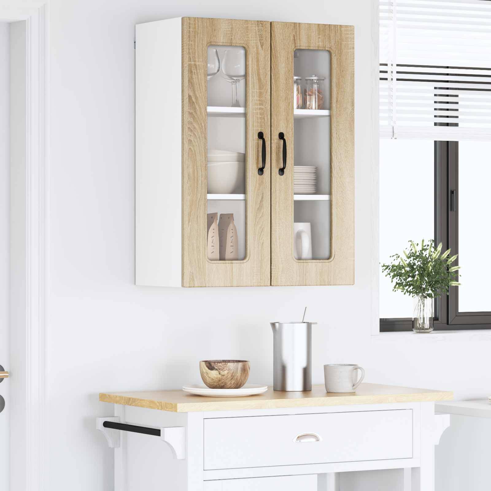 Wandhängende Küchenschränke mit Glastüren, in denen Gläser und Keramikbehälter ausgestellt sind. Darunter eine Arbeitsplatte mit einer Schüssel, einer Tasse und einem Wasserkocher. Eine kleine Pflanze steht in der Nähe des Fensters.