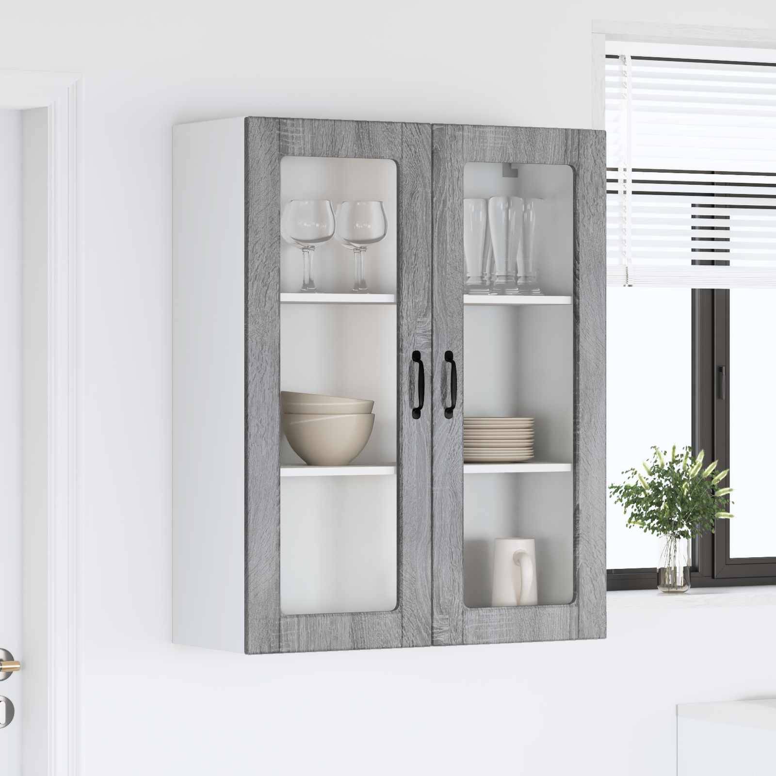 Ein wandhängender Küchenschrank mit Glastüren, der zwei Gläser, eine Schüssel und Teller enthält, neben einem Fenster mit teilweise geöffneten Jalousien.