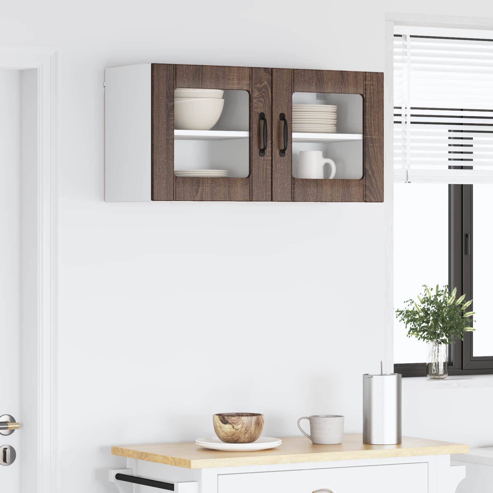 Kücheninterieur mit einem Holzschrank, zwei Glastüren, einer kleinen Pflanze auf der Fensterbank und Küchenutensilien auf der Arbeitsplatte.