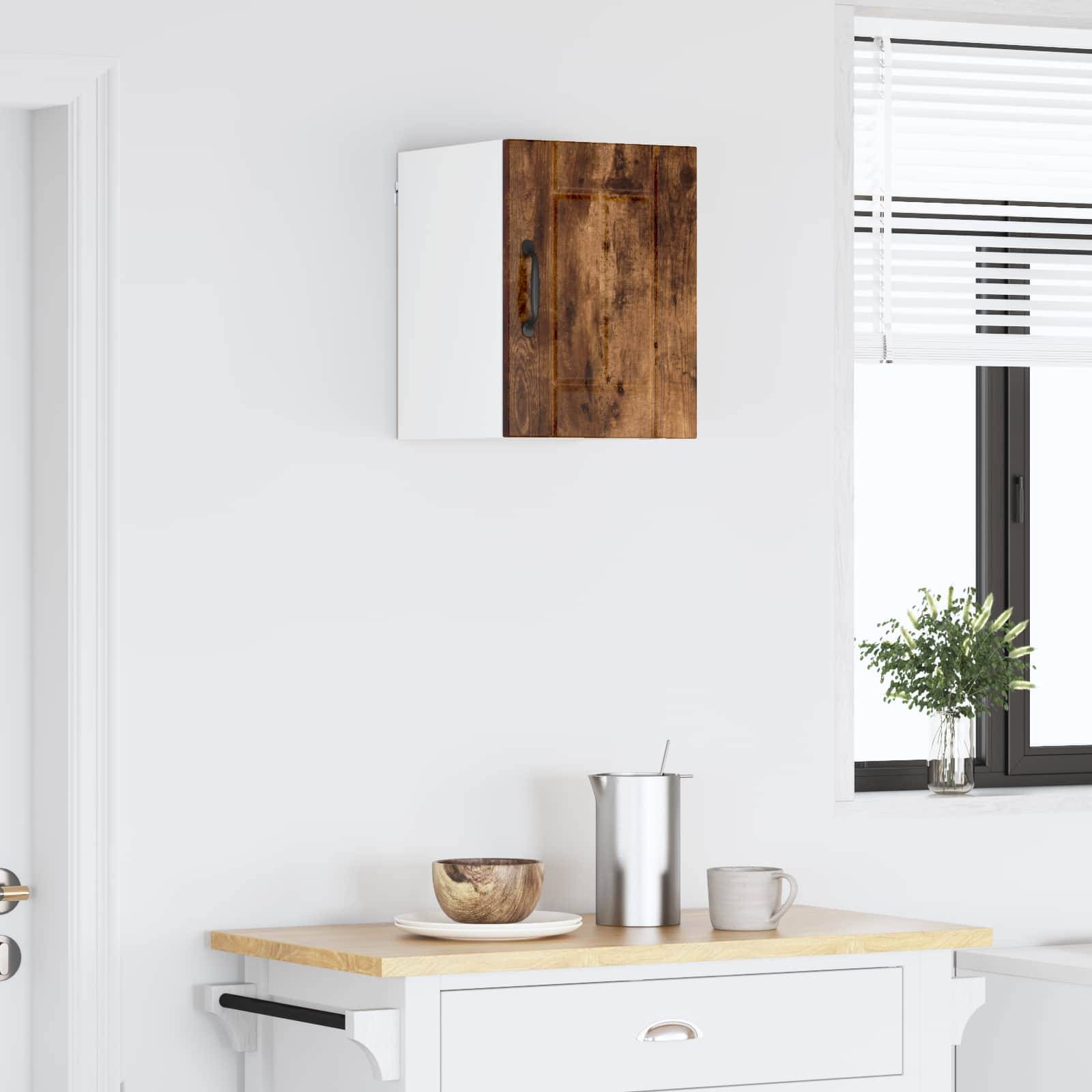 Eine minimalistische Küche mit einem weißen Schrank über einem Tisch, der eine Holzschale und einen Metallbecher enthält. Ein Fenster lässt natürliches Licht herein.