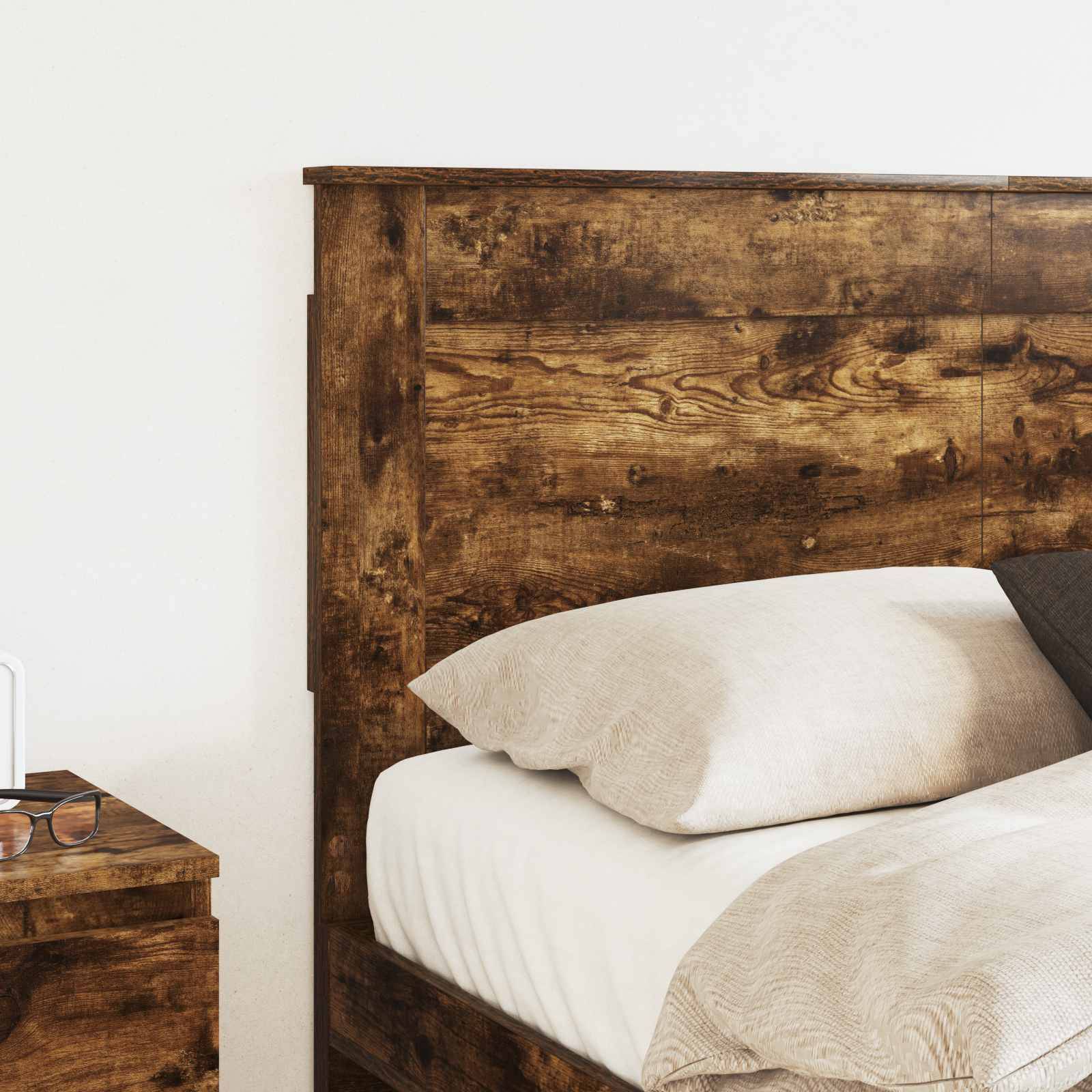 Ein Holzbett mit einem weißen Kissen und einer beigen Decke; auf der linken Seite ist ein kleiner Nachttisch mit einem Buch sichtbar.