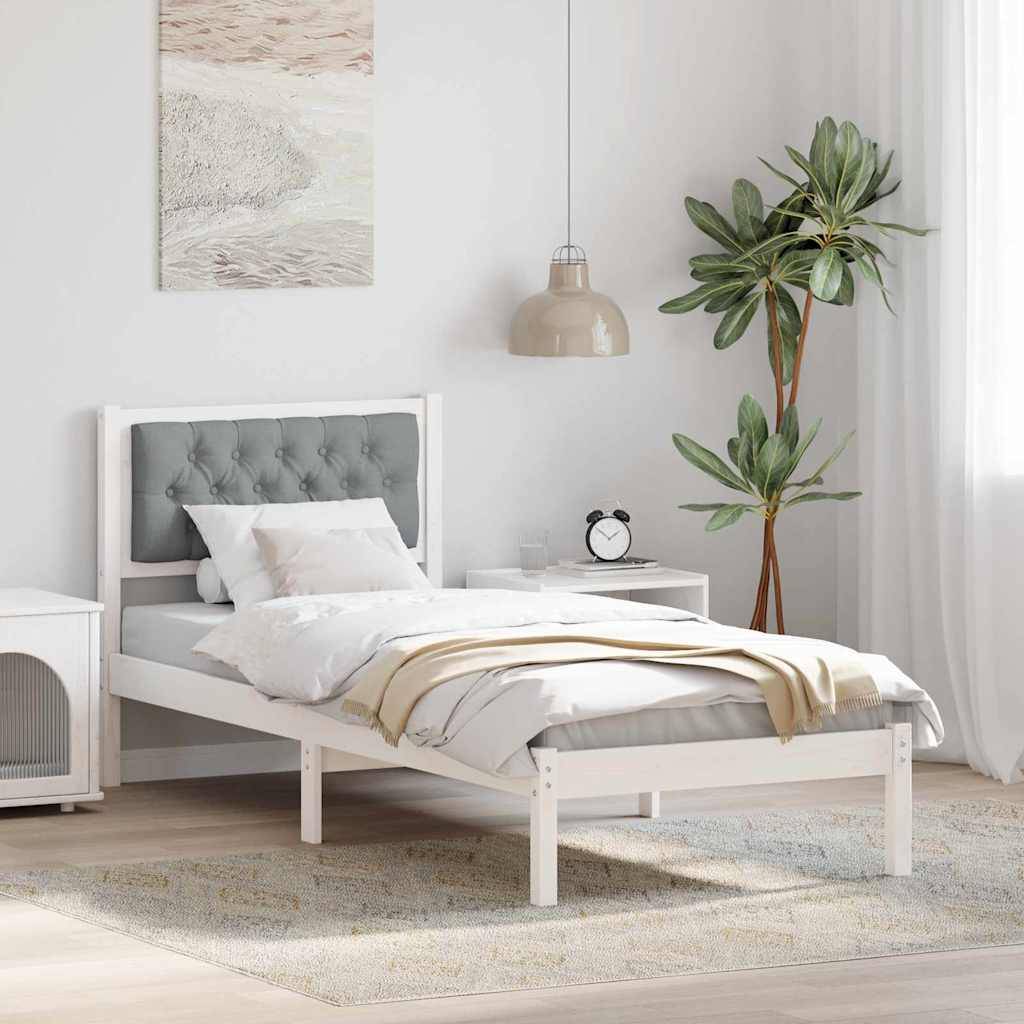 Ein minimalistisches Schlafzimmer mit einem weißen Bett, einem grauen Kopfteil und Kissen. Eine beige Pendelleuchte hängt über einem kleinen Nachttisch mit einer Pflanze.