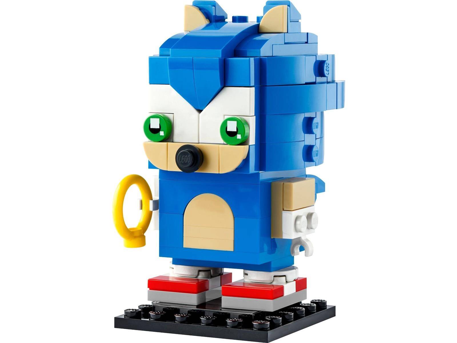 Eine kleine blaue LEGO-ähnliche Sonic-the-Hedgehog-Figur steht auf einem schwarzen Sockel, mit grünen Augen, roten Schuhen und einem gelben Ring in seiner Hand.