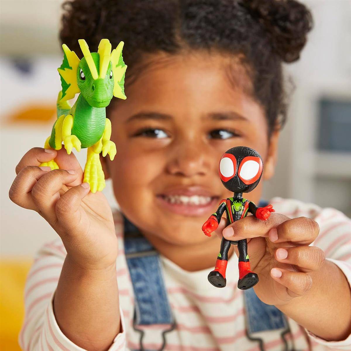 Lächelndes Kind, das zwei Actionfiguren in die Kamera hält – einen grünen Drachen und eine Spider-Man-ähnliche Figur.