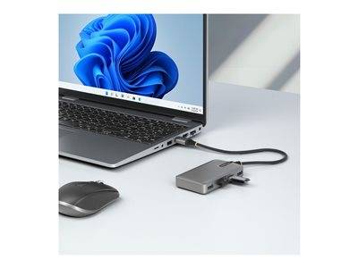 Ein Laptop, der mit einem Multi-Port-Adapter verbunden ist, steht auf einem Schreibtisch, neben einer Maus. Der Laptop-Bildschirm zeigt ein blaues abstraktes Design.