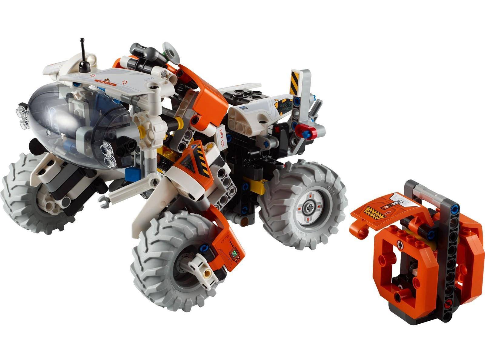LEGO-ähnliches orange und weißes Roboterfahrzeug mit Rädern und großen Reifen, dargestellt neben einer abnehmbaren orangefarbenen Komponente auf weißem Hintergrund.