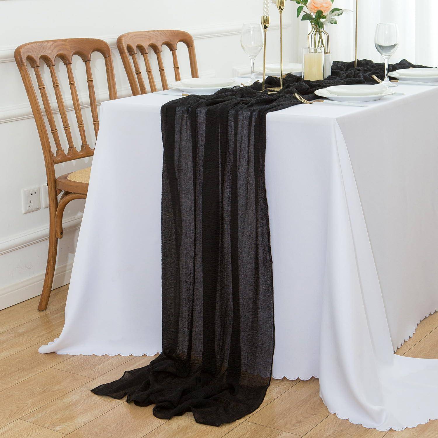 Ein Esstisch, gedeckt für zwei Personen, mit einem weißen Tischdecken und einem schwarzen Läufer, eleganter Tischware, Weingläsern und einem Blumenarrangement als Tischdekoration.
