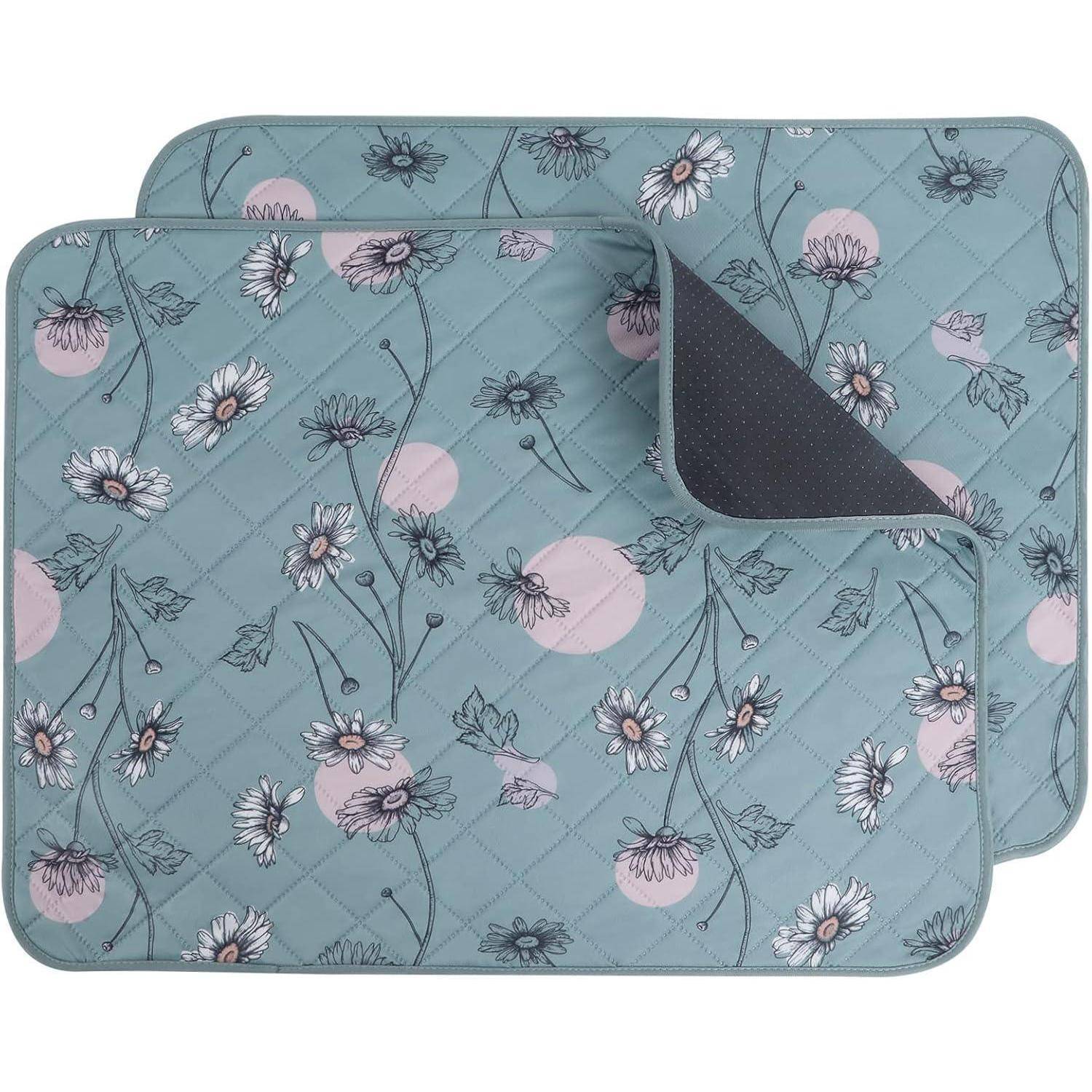 Zwei sich überlappende, blumengemusterte Matten auf einem blauen Hintergrund mit rosa Kreisen und weißen Blumen. Die Ecke der oberen Matte ist leicht umgeschlagen.