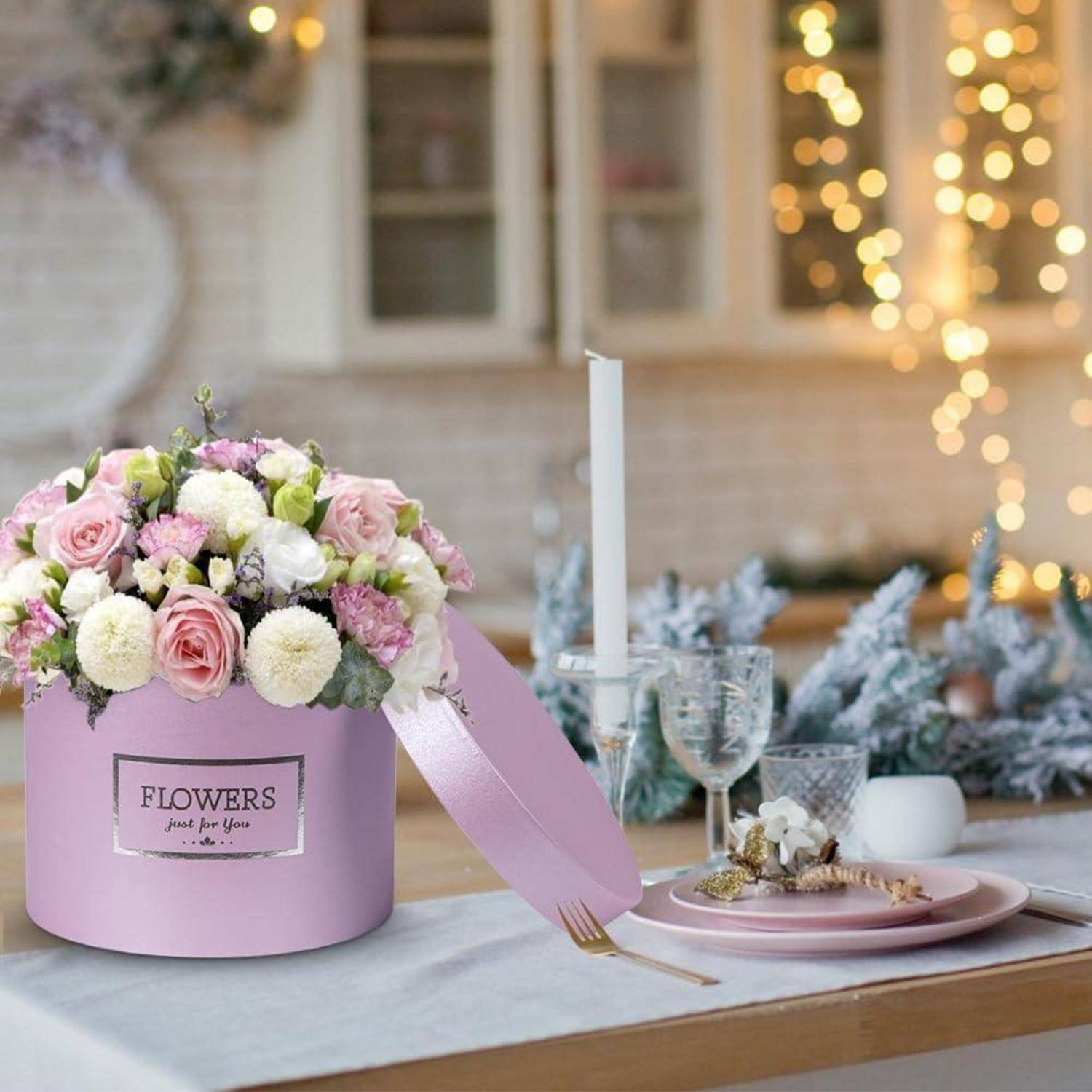 Eine runde rosa Schachtel mit der Aufschrift ‚BLUMEN nur für dich' auf dem Etikett, gefüllt mit weißen, rosa und lila Blumen, auf einem dekorierten Esstisch.