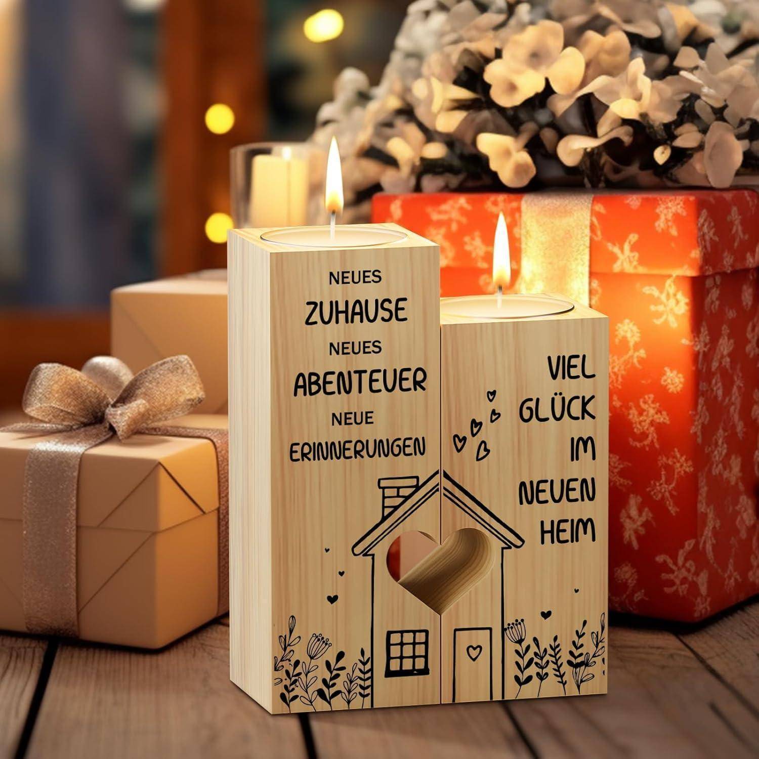 Zwei beleuchtete Kerzenhalter aus Holz, verziert mit tröstlichen Botschaften auf Deutsch über ein neues Zuhause, auf einem Tisch mit Geschenken und Blumen.
