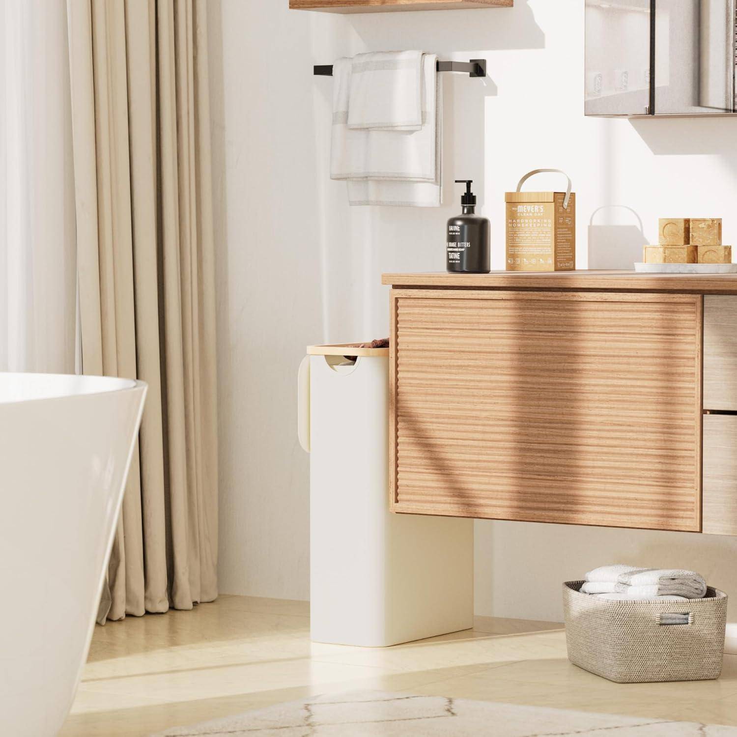 Modernes Badezimmer mit Holzwaschbeckenunterschrank, Waschbecken, Seifenspender, Handtuchhaltern, Badewanne und Korb. Sonnenlicht vom Fenster erzeugt eine warme Atmosphäre.