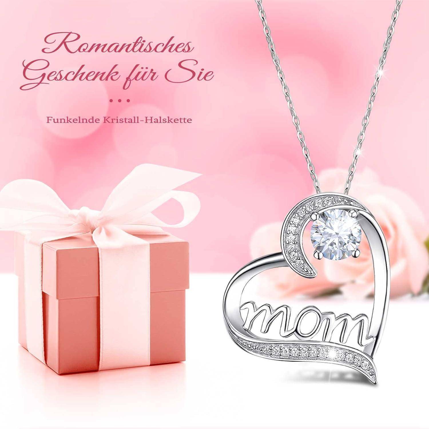 Eine herzförmige Halskette mit einem Kristall und dem Wort 'Mom', neben einer rosa Geschenkbox auf einem weichen rosa Hintergrund
