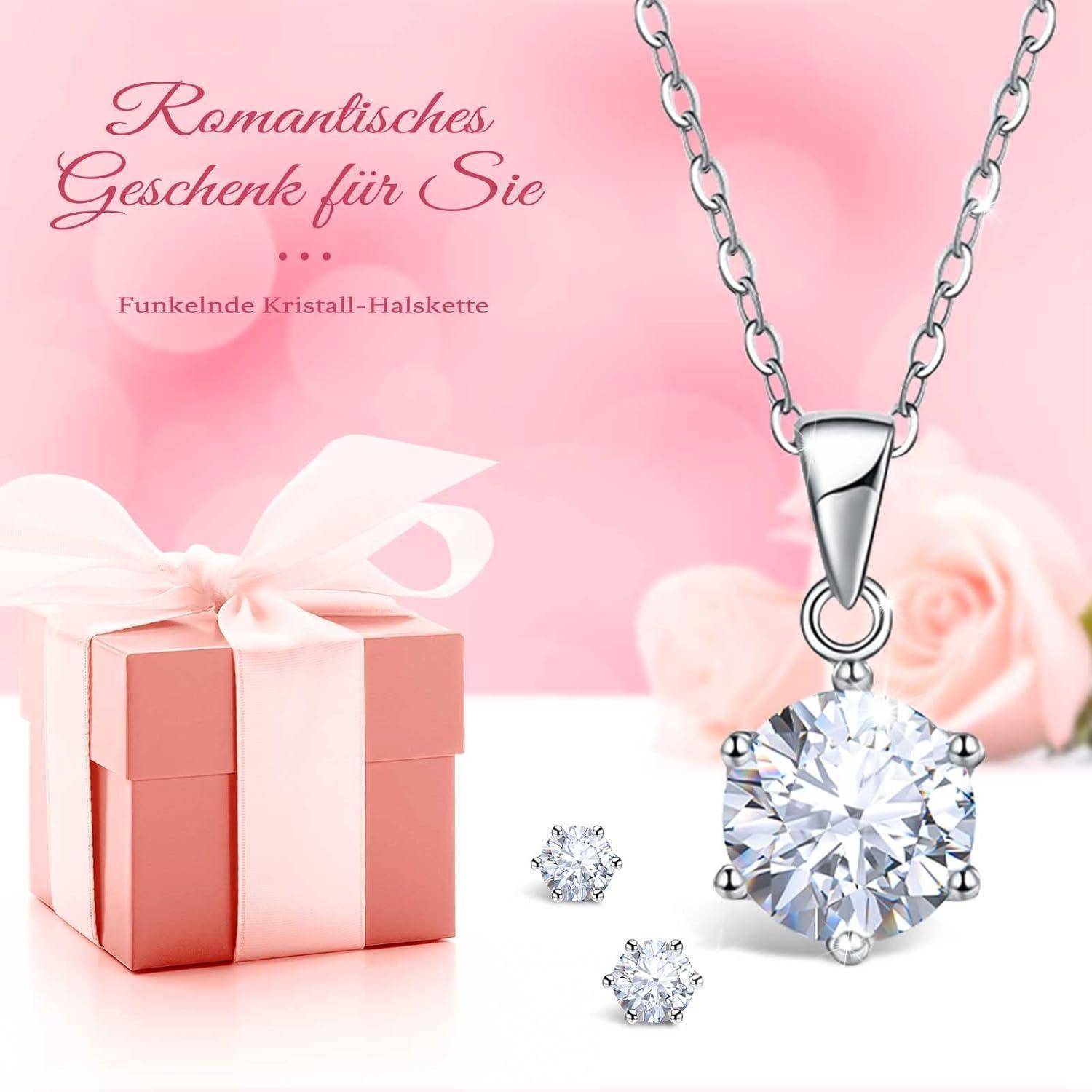 Eine Halskette mit einem großen Kristallanhänger und passenden Ohrringen wird vor einem rosa Hintergrund mit Rosen und einer Geschenkbox präsentiert.
