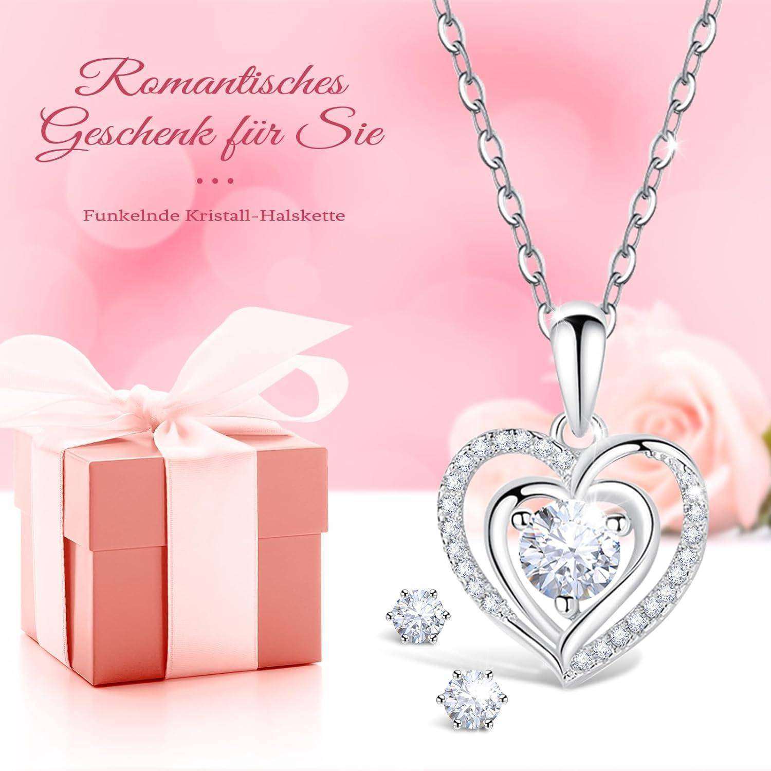 Eine silberne herzförmige Halskette mit einem zentralen Kristallanhänger, begleitet von kleinen Kristallohrringen und einer rosa Geschenkbox, vor einem Hintergrund von rosa Rosen.