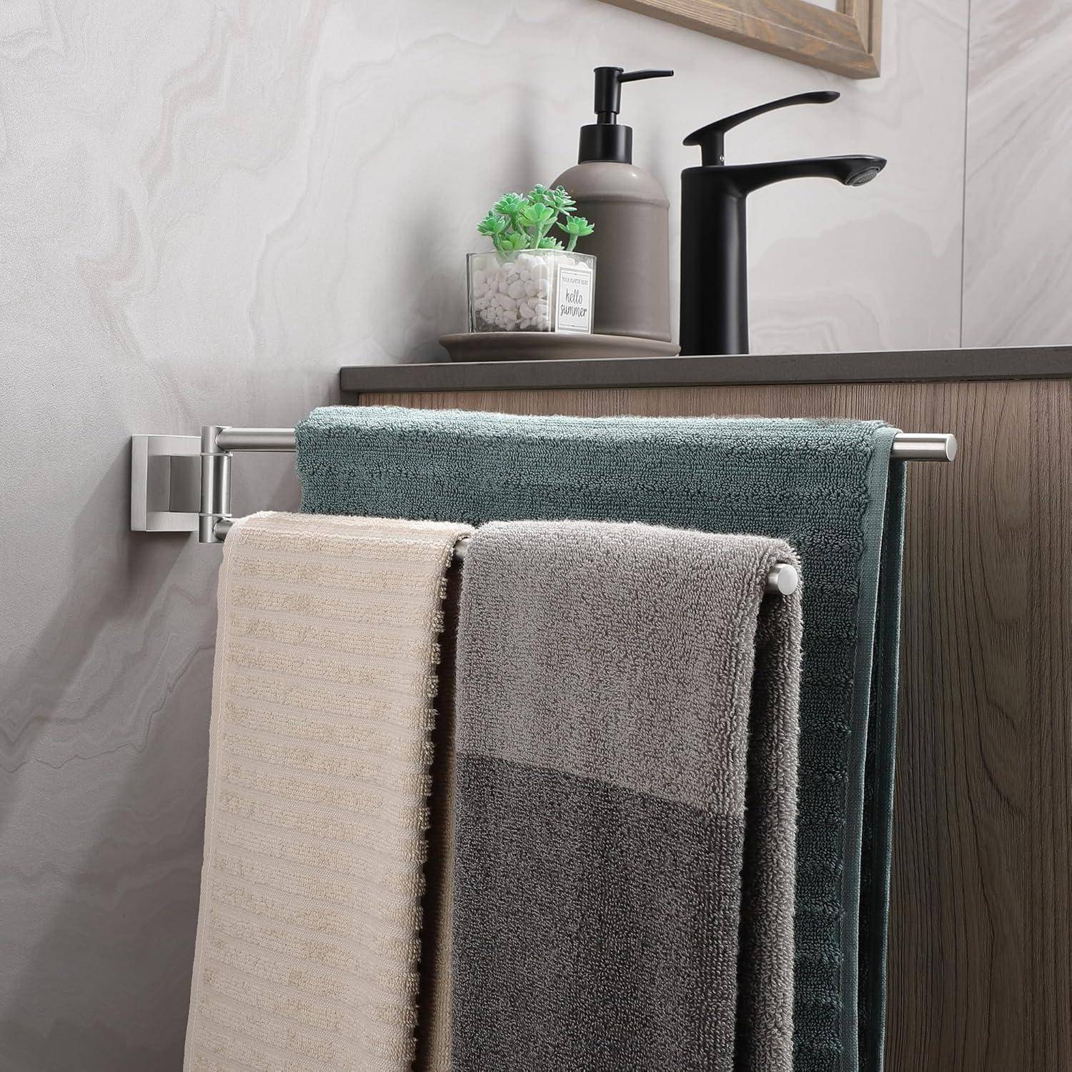 Handtücher in Beige, Grau und Petrol hängen an einem Ständer neben einem Waschbecken mit einem Seifenspender und einer Pflanze. Elegante, neutrale Einrichtung.