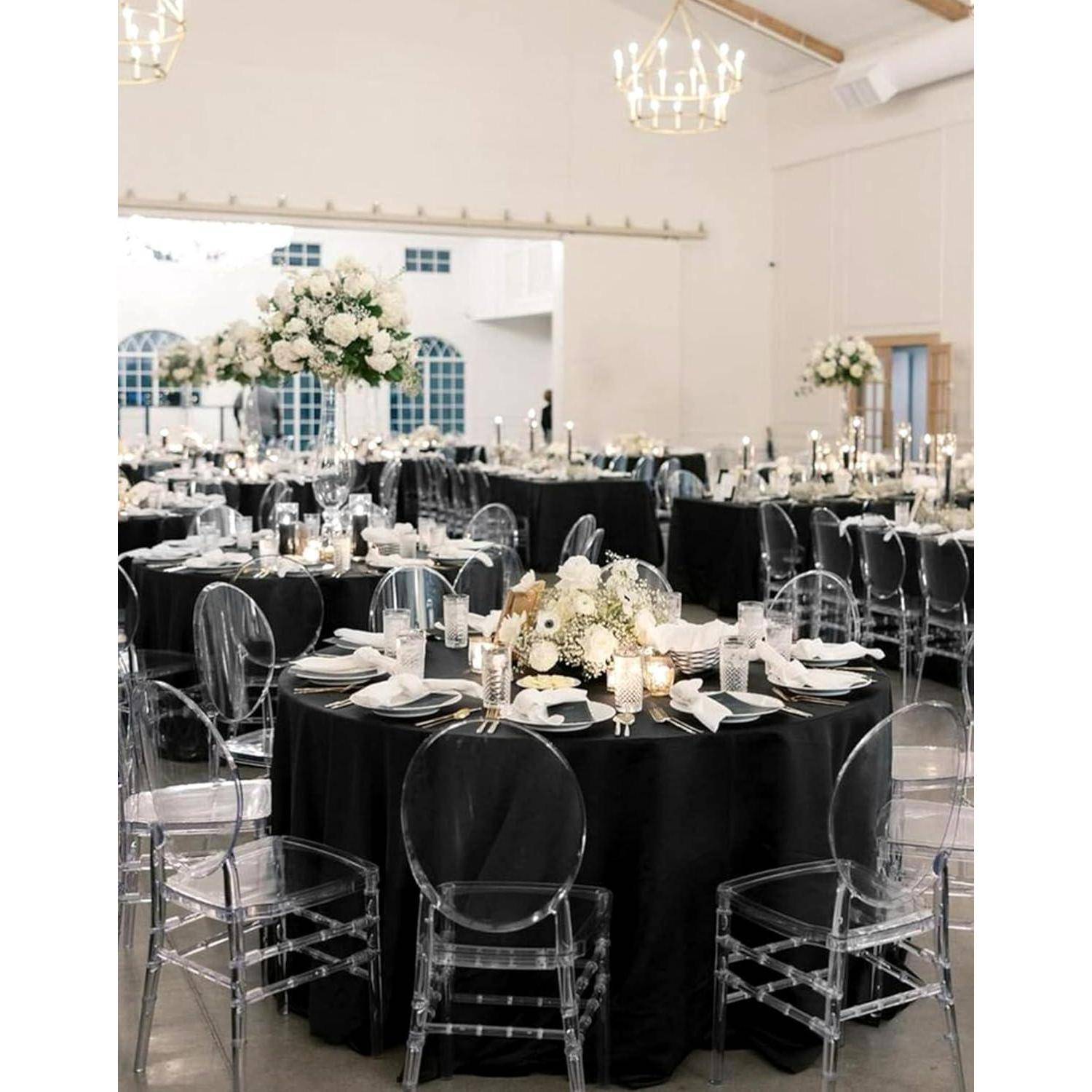 Elegantes Esszimmer-Arrangement für eine Veranstaltung mit runden Tischen, schwarzen Tischdecken, durchsichtigen Stühlen und Blumengestecken als Tischdekoration.
