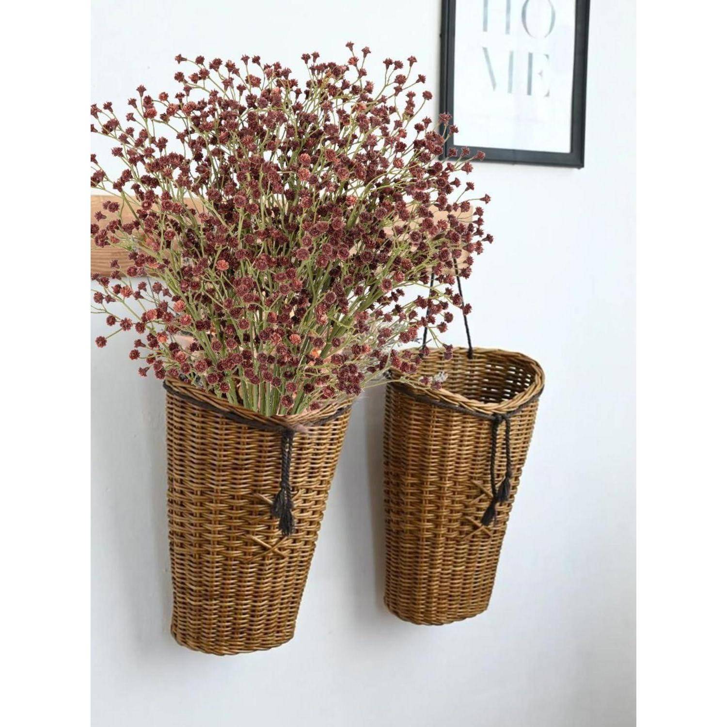 Zwei Flechtkörbe an einer Wand halten trockene rote Blumen, neben einem gerahmten Kunstdruck mit dem Wort 