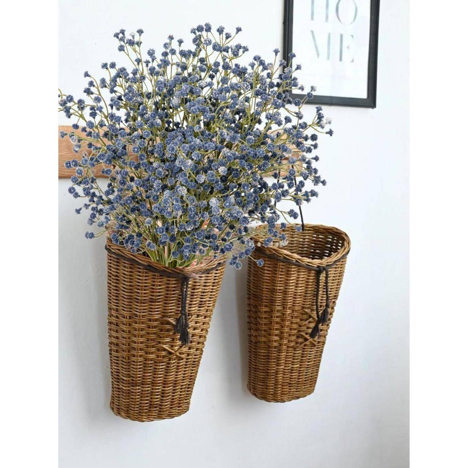 Zwei braune Flechtkörbe hängen an einer Wand; einer enthält einen Strauß kleiner lila Blumen. Ein gerahmter Druck zeigt die Aufschrift 