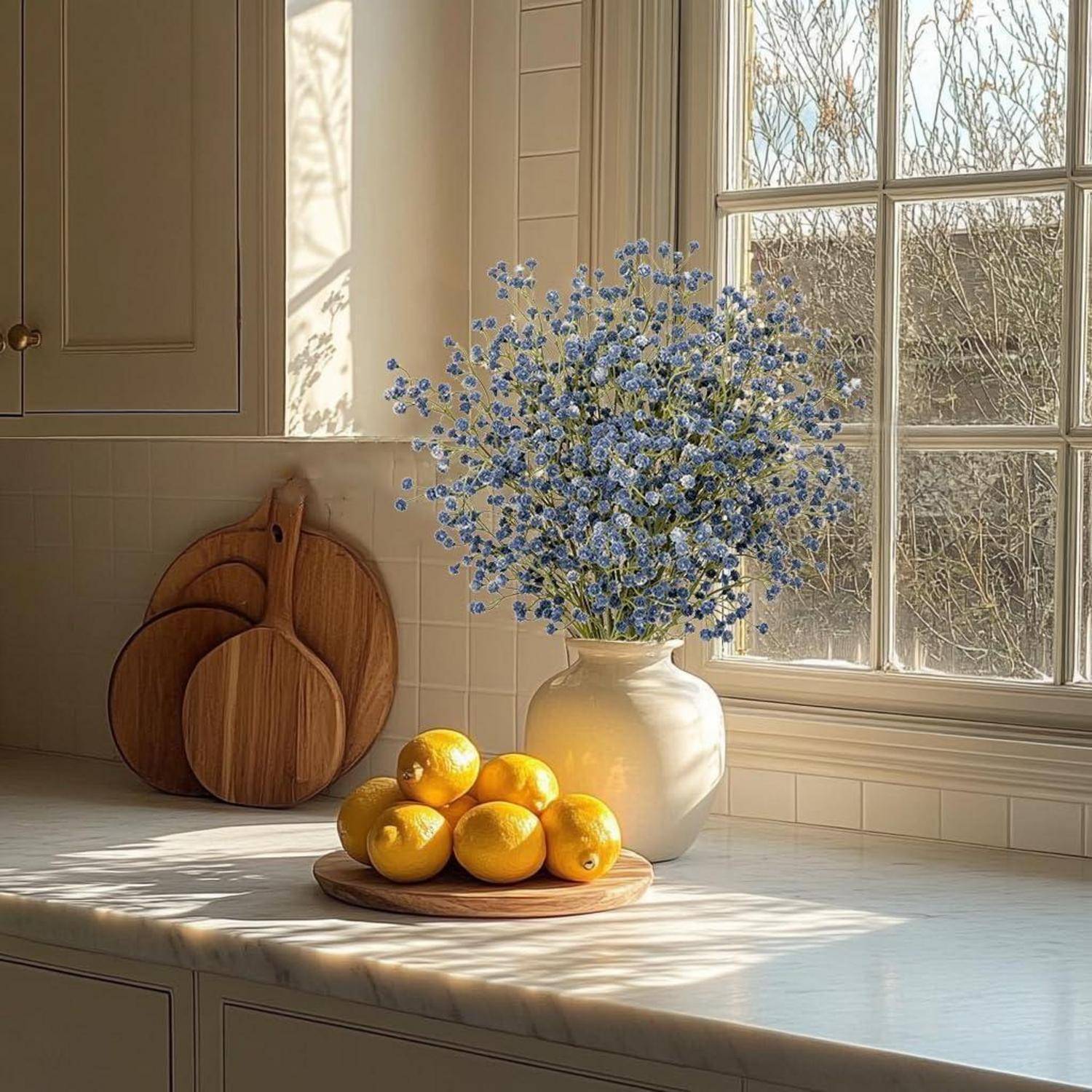 Eine von Sonnenlicht durchflutete Küchenarbeitsplatte mit einer Vase blauer Blumen und einem Holztablett mit Zitronen. Zwei Schneidbretter lehnen an der Rückwand.