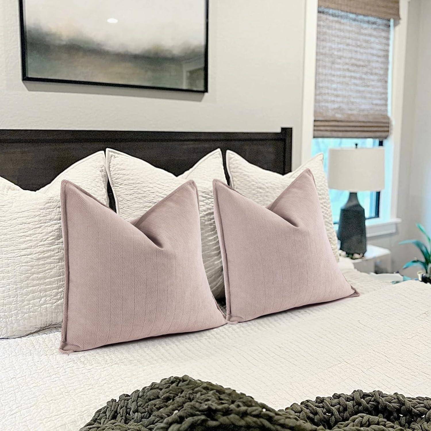 Ein ordentlich gemachtes Bett mit weißen Laken und zwei großen, rosa Kissen im Vordergrund. Ein schwarzes Kopfteil und ein Gemälde darüber vervollständigen die Dekoration.
