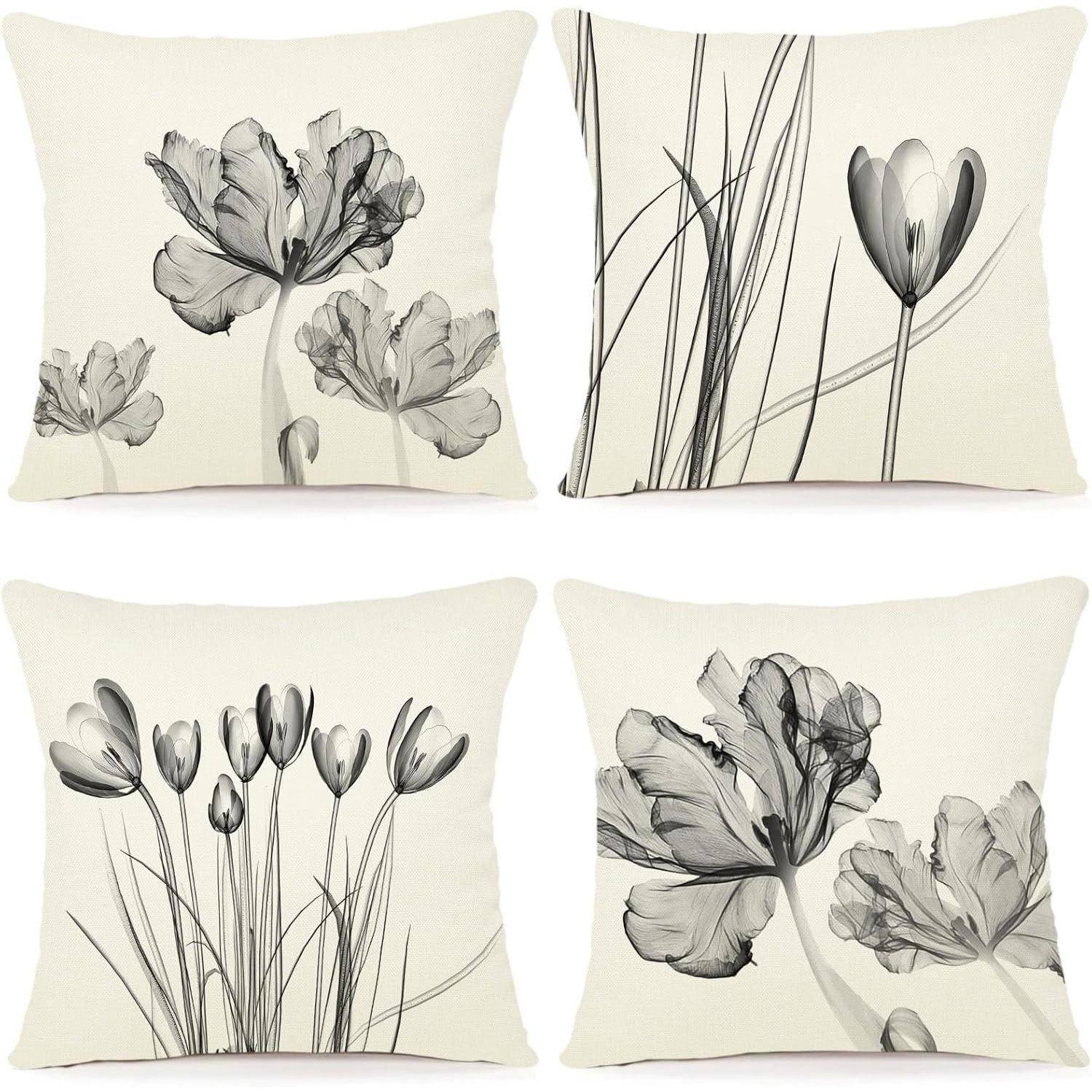 Vier quadratische Kissen mit Floral-Designs in Grautönen, die jeweils unterschiedliche Blumen- und Grasstile auf einem hellen Hintergrund präsentieren.