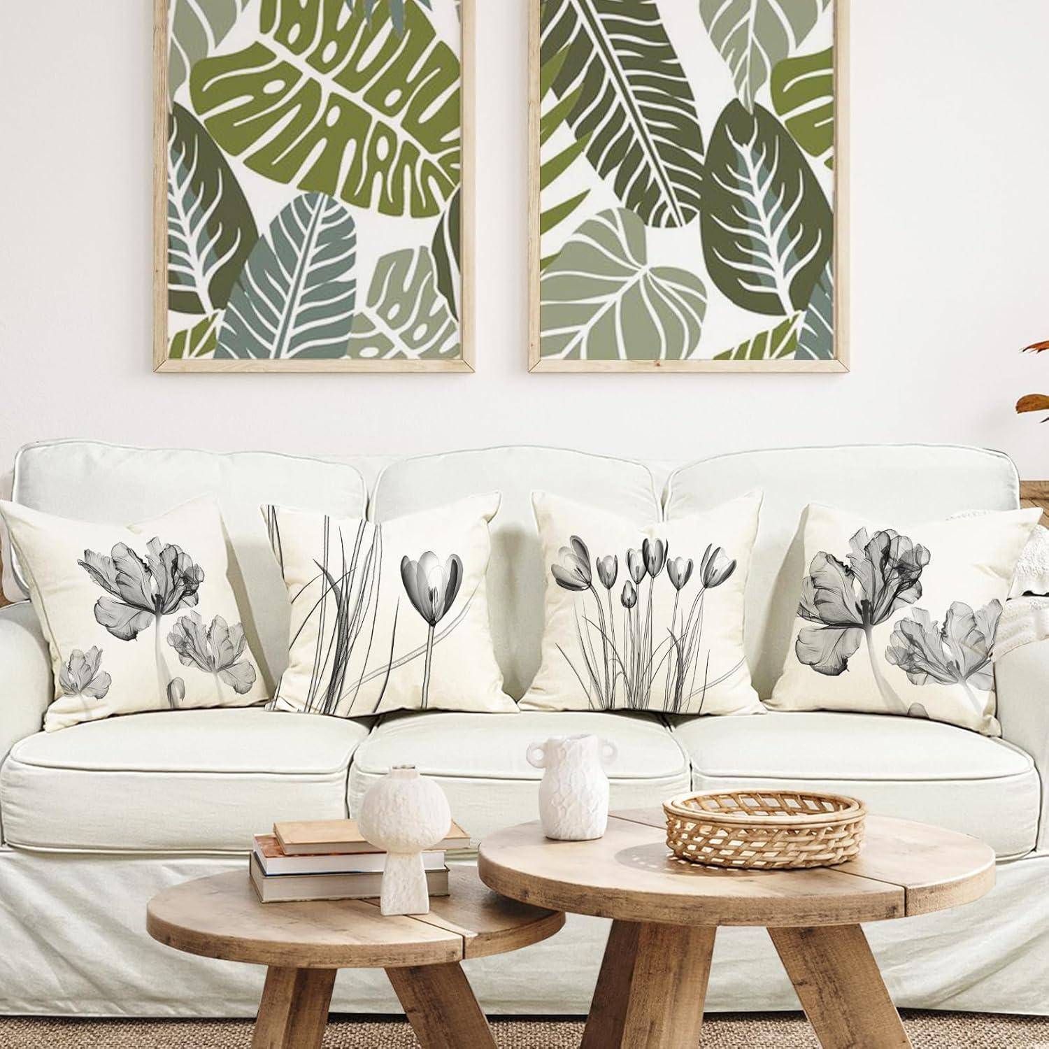 Ein weißes Sofa mit blumenmusterverzierten Kissen steht vor einer Kunstarbeit mit tropischen Blättern. Auf dem Holzkaffeetisch befinden sich dekorative Gegenstände.