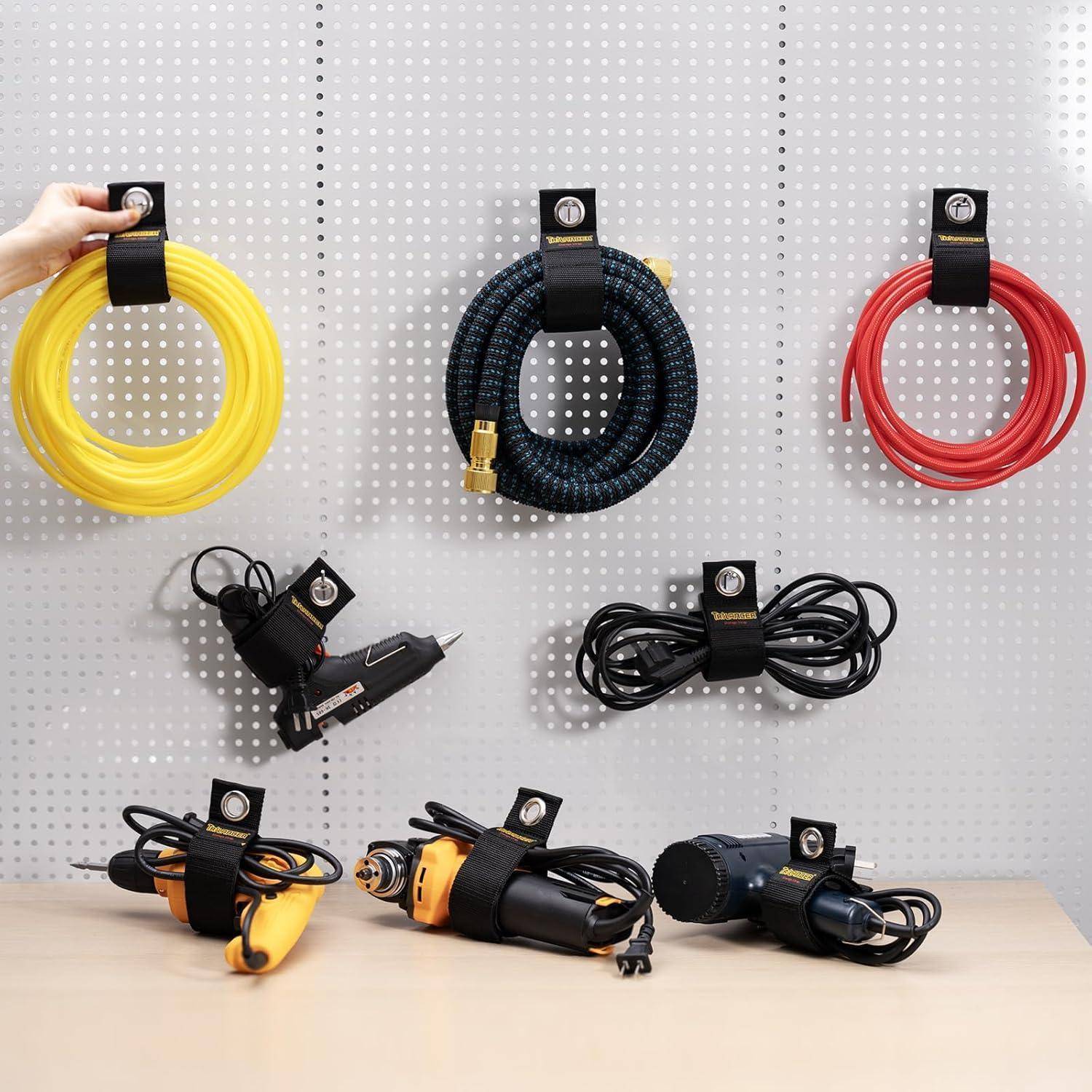 Verschiedene Kabel und Werkzeuge sind übersichtlich an einer Lochplatte angeordnet, darunter gelbe, schwarze und rote aufgewickelte Kabel, eine Klebepistole und Elektrowerkzeuge.