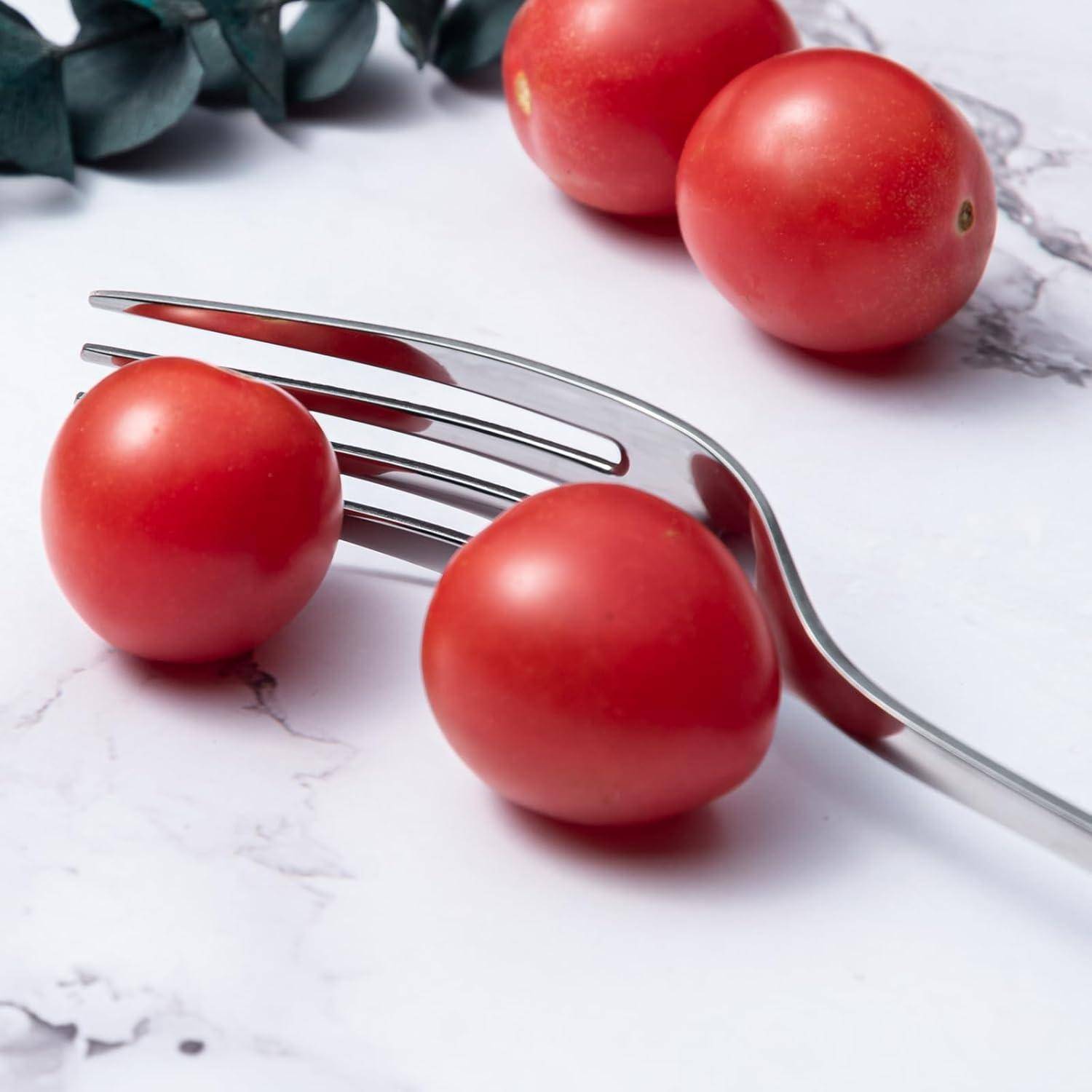 Drei Kirschtomaten auf einer Marmoroberfläche neben einer silbernen Gabel, mit grünen Blättern im Hintergrund.