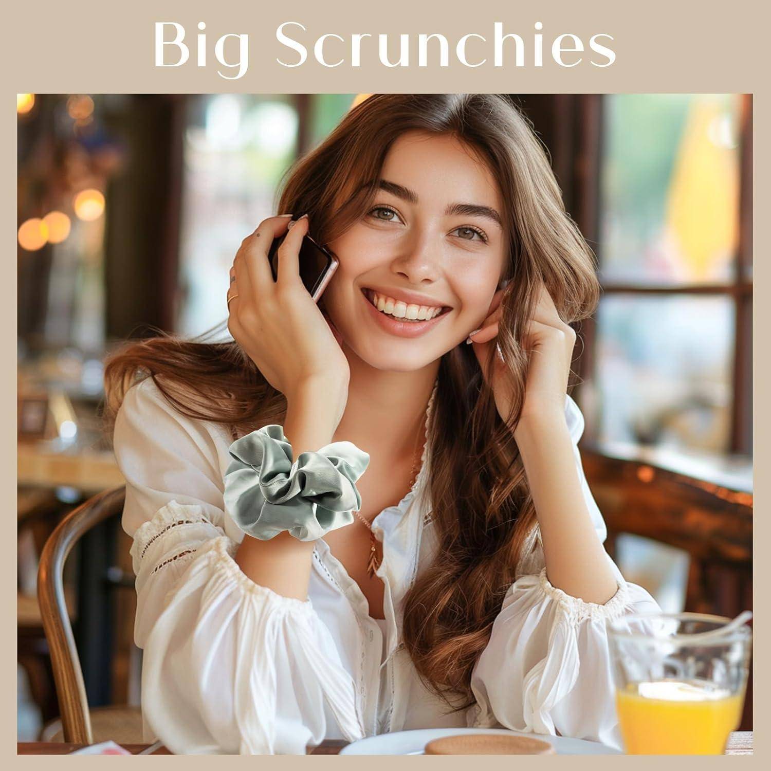 Eine Frau mit langen braunen Haaren lächelt, während sie in einem Café telefoniert. Sie trägt eine weiße Bluse und einen großen Scrunchie am Handgelenk.