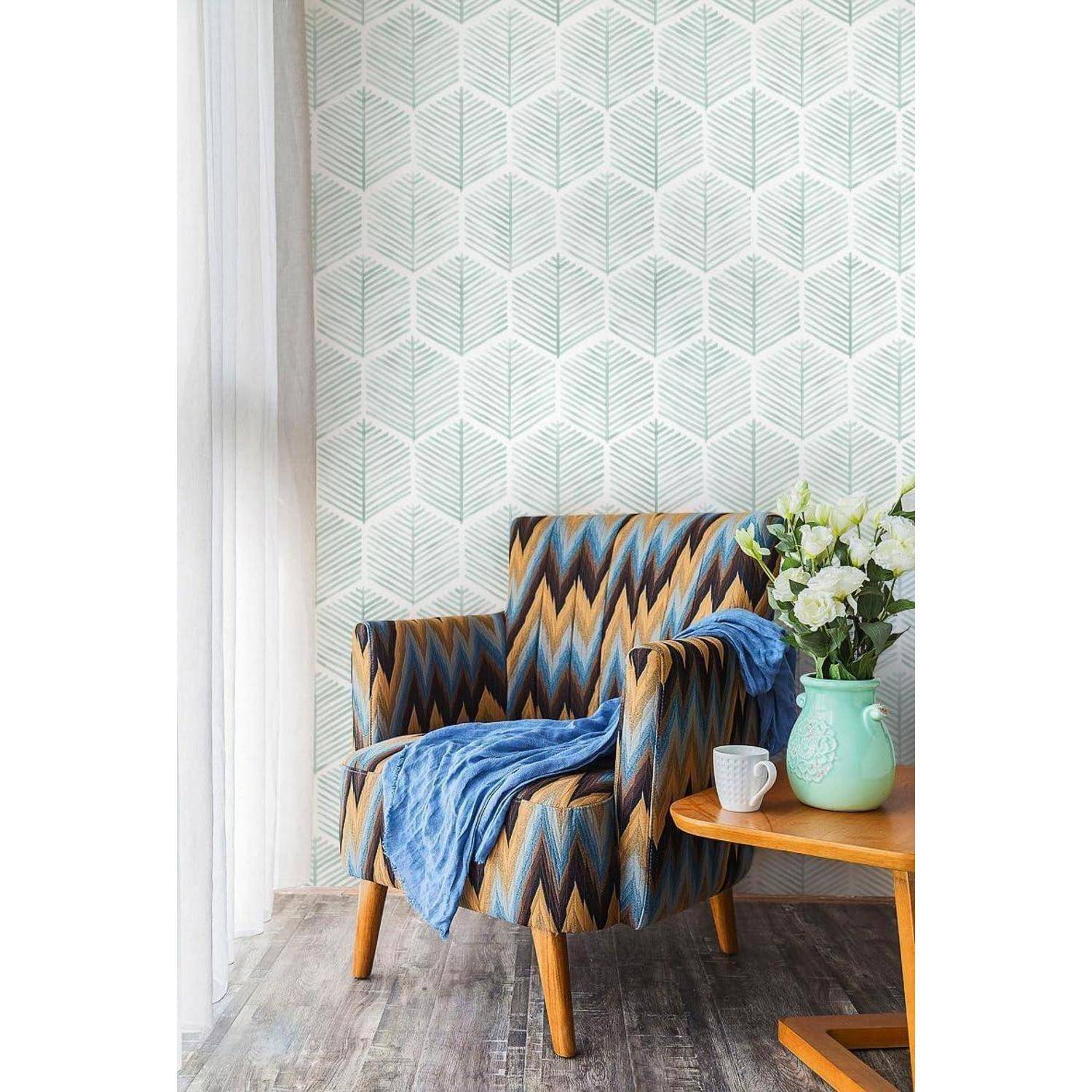 Ein gemusterter Sessel mit einem blauen Schal, der darüber drapiert ist, neben einem kleinen Holztisch mit Blumen in einer Vase und einem weißen Becher, vor einer geometrischen Tapete.