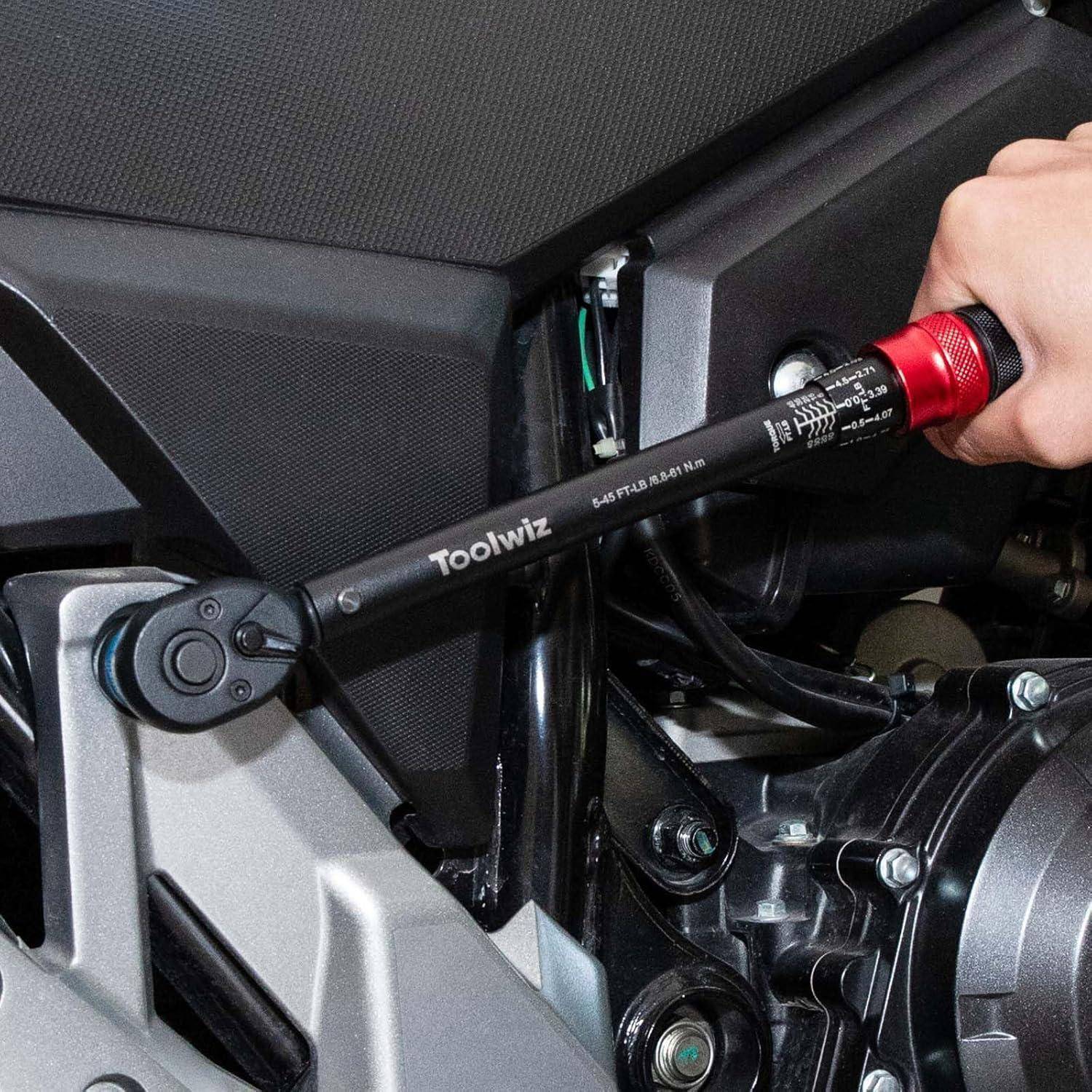 Eine Person verwendet einen roten und schwarzen Drehmomentschlüssel, um eine Schraube am Motorrad-Motor einzustellen, wobei der Fokus auf Präzision liegt und die Beschriftungen am Werkzeug sichtbar sind.