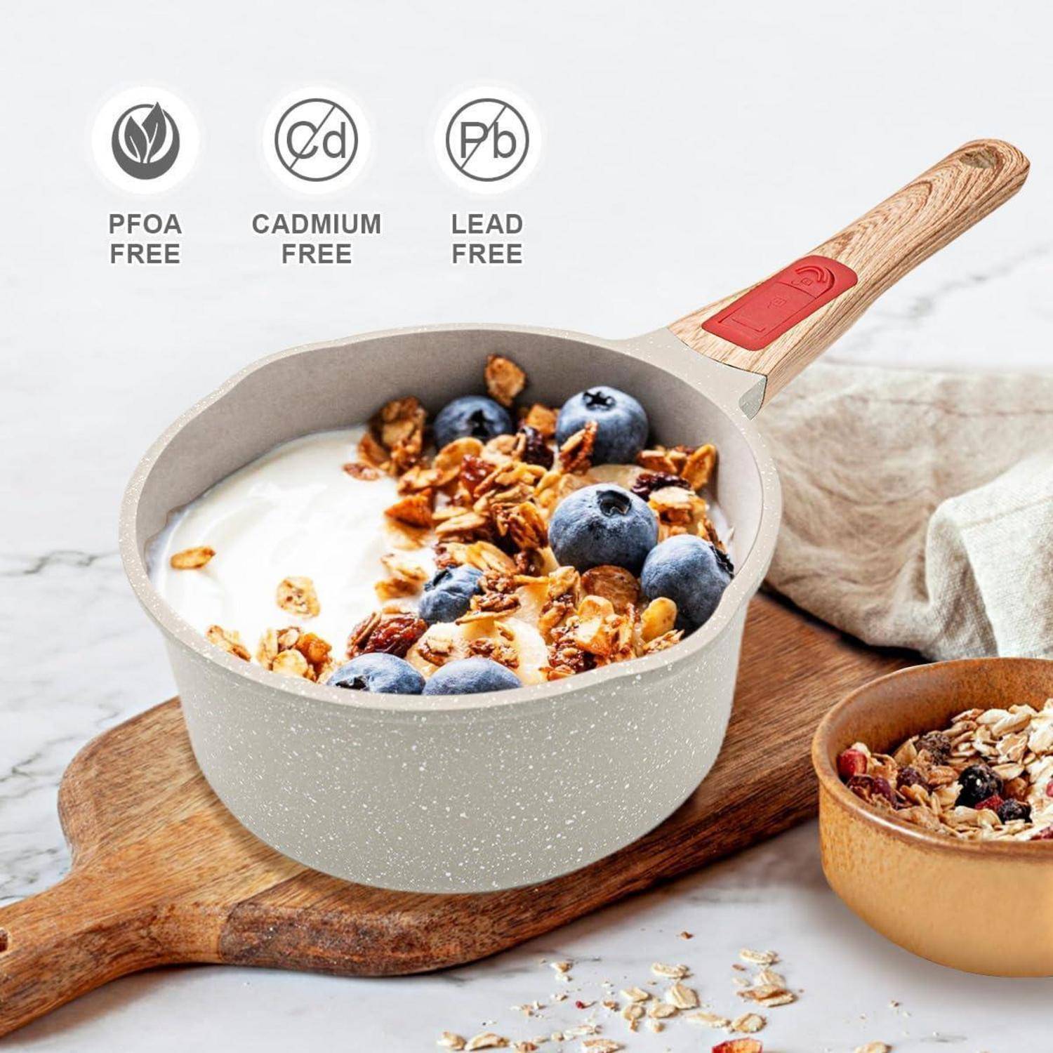 Ein Topf Joghurt, mit Blaubeeren und Granola bedeckt, wird auf einem Holzbrett platziert, daneben steht eine kleine Schüssel mit ähnlichem Inhalt. Der Topf ist mit den Aufschriften „PFOA-frei
