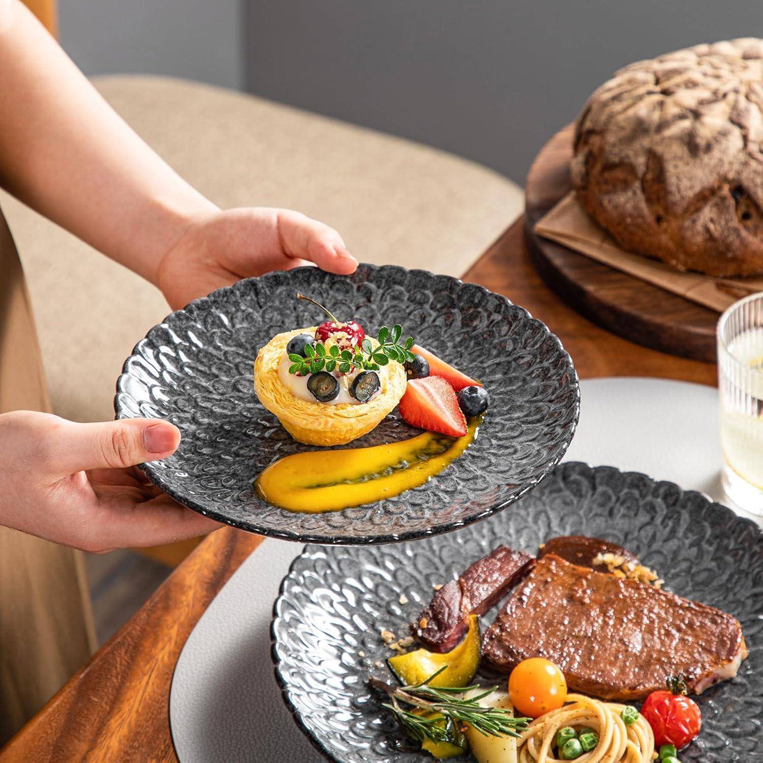 Eine Person serviert ein Dessert mit Blaubeeren und Sauce auf einem Teller, neben einem anderen Teller mit Steak und Gemüse auf einem Esstisch.