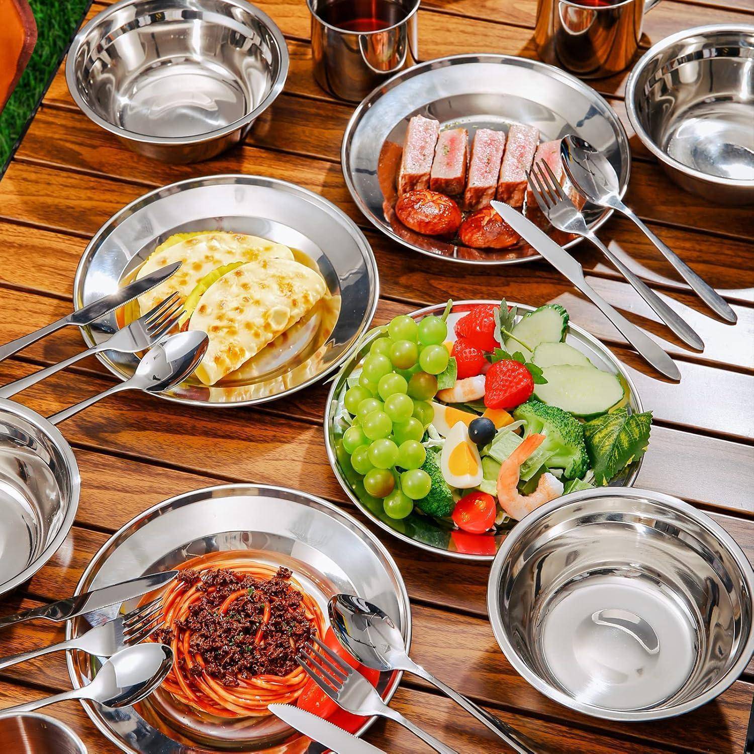 Ein für eine Mahlzeit gedeckter Tisch mit Schalen voller Käse, Würstchen, Trauben, Erdbeeren, Gurken und einer Nudelgerichtplatte, angeordnet auf glänzenden Tellern.