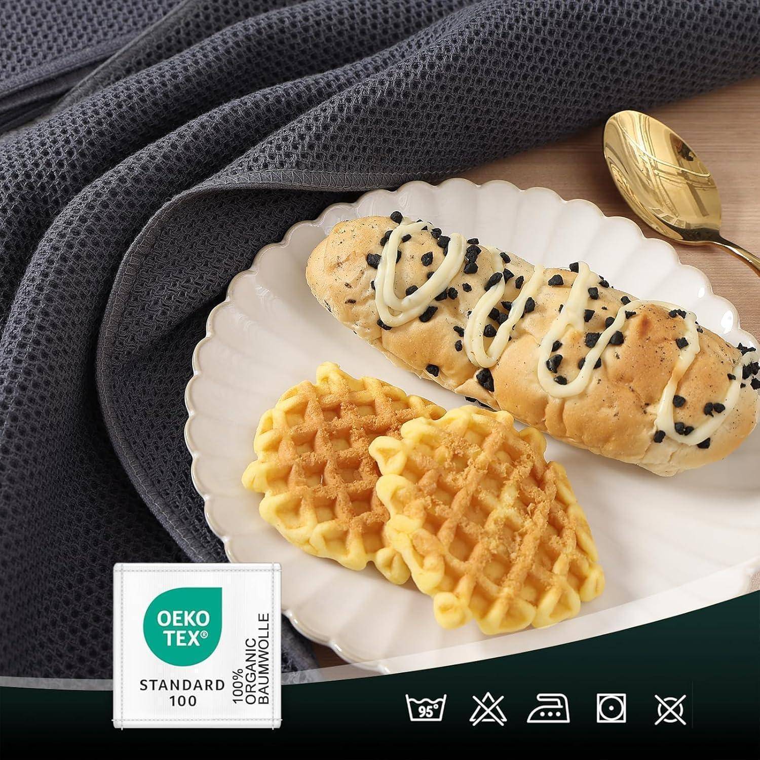 Teller mit Mandel-Croissant und zwei Waffeln auf einer schwarzen Oberfläche, daneben eine Gabel und eine Serviette mit der Aufschrift 