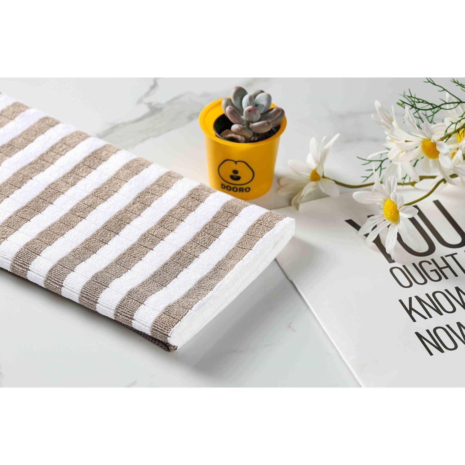 Ein gestreiftes Handtuch auf einer Marmoroberfläche, neben einem kleinen gelben Topf mit einer Sukkulente und weißen Gänseblümchen. Ein Teiltext liest sich 