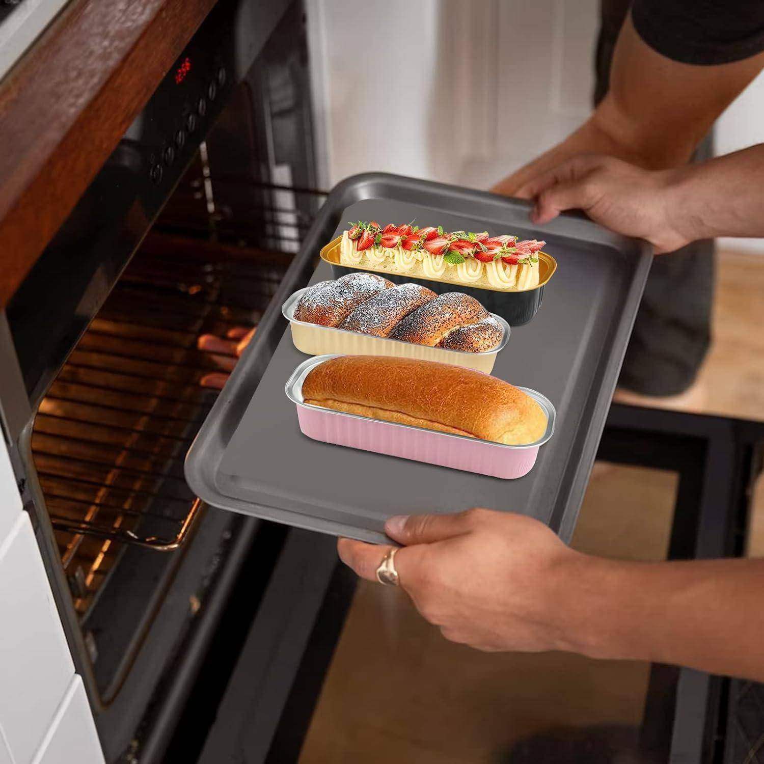 Eine Person stellt ein Tablett mit drei verzierten Kuchen in einen Ofen. Die Kuchen befinden sich in pastellfarbenen Backformen, und der Ofen ist geöffnet und bereit.