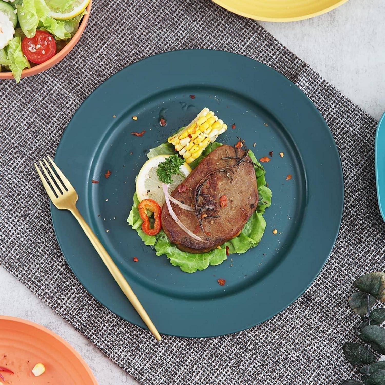 Ein Teller mit in Scheiben geschnittenem Fleisch, Mais, Salat und einer roten Paprika, garniert mit Kräutern auf einem strukturierten Platzdeckchen, begleitet von einer goldenen Gabel.